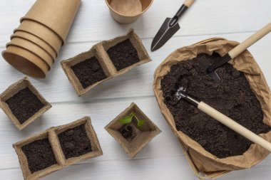 Garden tool in a paper bag with soil. Peat and paper pots with soil. Flat lay.  White background.