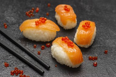 Sushi with salmon and red caviar, chopsticks. Caviar on the table. Top view.  Black background.