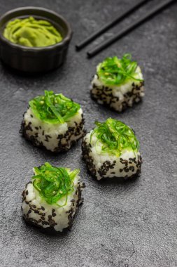 Sushi with green algae. Food sticks. Wasabi in a black bowl. Top view.  Black background
