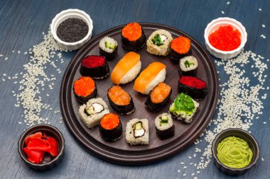 Different types of sushi on a round board. Rice is scattered on the table. Seasonings in bowls. Top view. Blue background