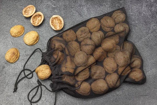 Whole walnuts in a black mesh resealable bag. Nut shell on the table. Flat lay. Black background