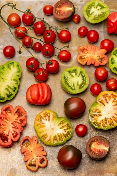 Different types of tomato, tomato halves and a sprig of cherry tomatoes. Flat lay. Rusty background.