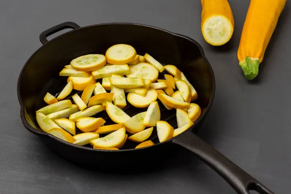 Two whole yellow zucchini. Sliced yellow zucchini in a frying pan. Top view. Gray background.