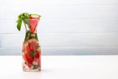 Bir sürahi suda karpuz dilimleri ve bir tutam yeşil fesleğen. Uzayı kopyala Beyaz arkaplan.