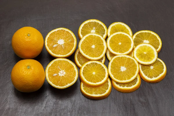 Two whole oranges, sliced orange on a brown background. Flat lay