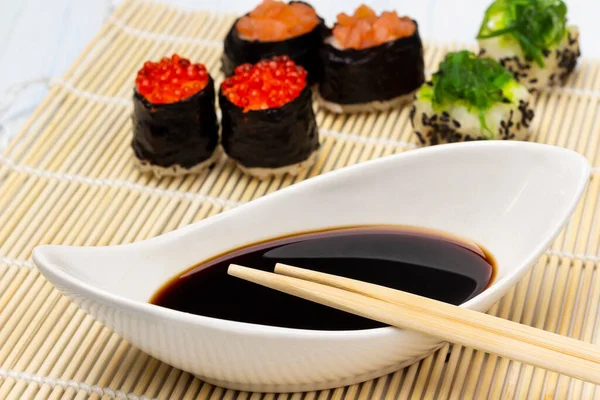 stock image Chopsticks on a bowl with soy sauce. Sushi with caviar and seaweed on a bamboo sushi mat. Close up.