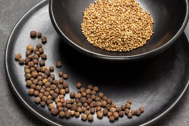 Siyah porselen tabakta Allspice. Siyah kasede kişniş tohumları. Kapatın. Üst Manzara. Siyah arkaplan