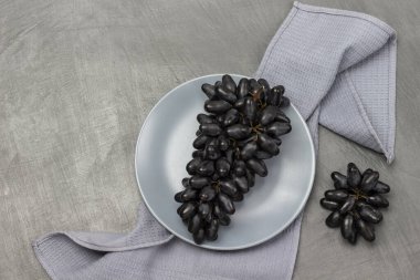 Gri bir tabakta bir demet siyah üzüm. Peçete masanın üzerinde. Gri arkaplan.