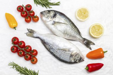 Sebzeli taze dorado balığı. Kırmızı domates, renkli biber, yeşil biberiye, beyaz arka planda limon. Düz yatıyordu