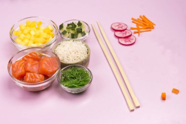 Çiğ sebze, kırmızı balık, pirinç, cam kaselerde soya sosu. Hawai yemeği. Pembe arka planda bambu çubuklar. Üst görünüm