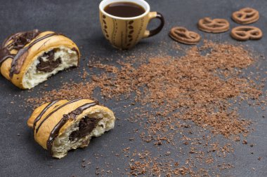 Çikolatalı iki parça kruvasan, bir fincan kahve, çikolata parçacıkları. Siyah arka plan. Üst Manzara. Boşluğu kopyala