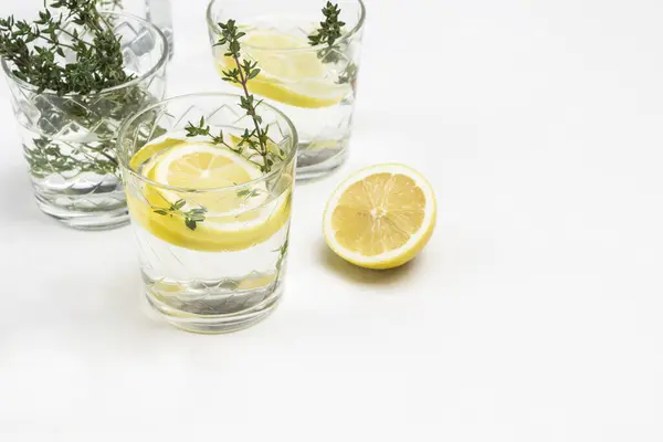 Lemon drink in glass. Thyme sprigs in glass. Lemons on table and in ceramic bowl. Close up. White background. Top view