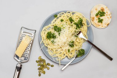Brokolili spagetti, çatal, çatal ve kaşık seramik tabakta. Parmesan peyniri ve rende. Flatekmekler masada. Gri arka plan. Düz yatıyordu