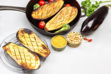 Grilled eggplants on wire rack and in pan with vegetables and groats. White background. Flat lay