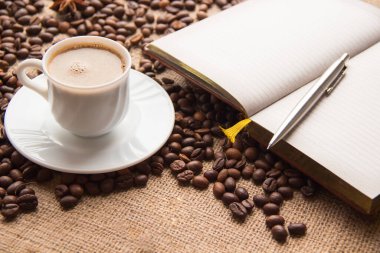 Bir fincan kahve, kavrulmuş tahıllar, masada açık defter ve kalem.