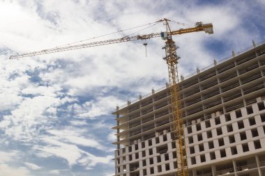 İnşaat kulesi vinci ve tamamlanmamış bina. Bulutlarda gökyüzü.