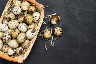 Hasır sepette bıldırcın yumurtası. Yumurta ve tüy masada. Siyah arka plan. Düz yatıyordu. Boşluğu Kopyala