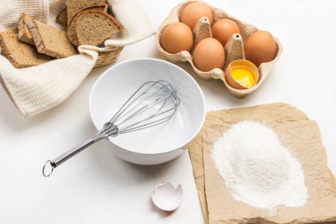 Kasede çırpın. Kağıt üzerinde un. Karton kutuda yumurtalar. Beyaz peçetede tost. Beyaz arka plan. Üst yaşam