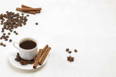 Bir fincan kahve, tarçın çubukları ve çay tabağında yıldız anason. Masada kahve ve tarçın taneleri var. Beyaz arka plan. Üst Manzara. Boşluğu Kopyala