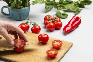 Elleri bıçakla kesilmiş kırmızı biber. Masada domates ve ıspanak yaprakları var. Gri arka plan. Üst görünüm