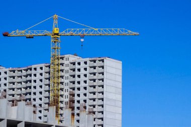 Bir inşaat vinci ve mavi gökyüzünün arka planına karşı beton panellerden yapılmış bir binanın tamamlanmamış inşaatı..