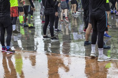 Sporcular yağmurda ıslak bir pistte dururlar. Su birikintilerindeki ayak yansımaları. Çerçevenin bir parçası