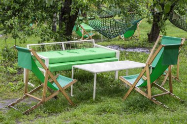Katlanmış ahşap sandalyeler, bir yaz koltuğu ve bahçede çimenlikte bir masa. Parktaki dinlenme alanı.