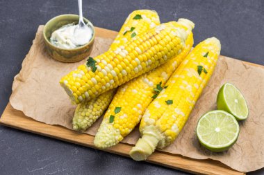 Tahtada haşlanmış mısır. Limon ve sos kasede. Maydanoz yaprakları. Siyah arka plan. Üst görünüm