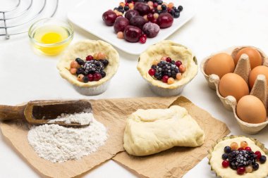 Donmuş böğürtlenlerden pasta yapmak. Kağıt üzerinde un ve hamur. Hamur ve böğürtlen kabında. Beyaz arka plan. Üst görünüm