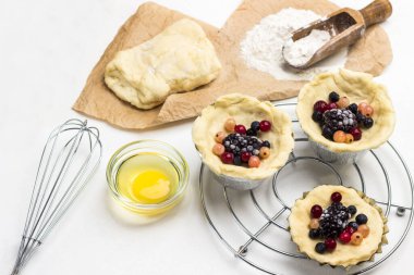 Hamur ve böğürtlen, metal işlemeli kabın içinde. Yumurta sarısı ve çırpma kabı. Kağıt üzerinde un ve hamur. Beyaz arka plan. Üst görünüm