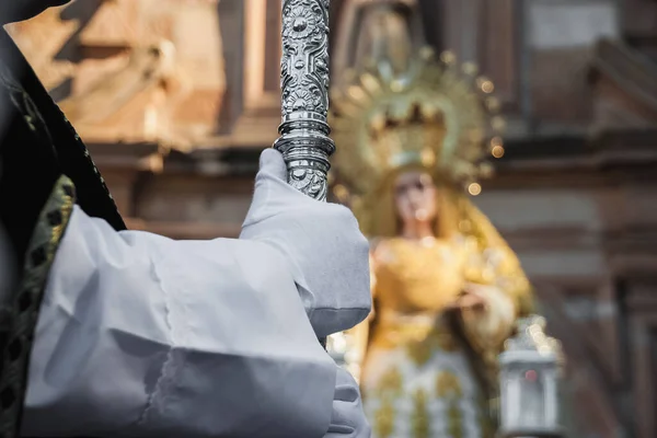 A priest wearing a white robe is holding a statue of a woman in a white robe.