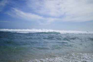 Sahildeki deniz dalgaları ve parlak mavi bulutlar, güzel sahil manzarası.