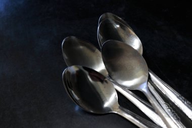 Bir ev ve restoranda mutfak masasında siyah bir arka plana karşı kaşık yığını.