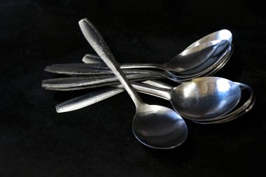 Bir ev ve restoranda mutfak masasında siyah bir arka plana karşı kaşık yığını.