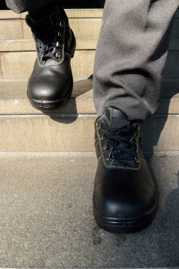 Ayaklarını korumak için iş yerinde siyah deri ayakkabılar giyen bir inşaat işçisinin fotoğrafı.