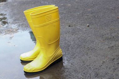 Su birikintisindeki sarı lastik botların fotoğrafı, bu ayakkabılar genellikle işçiler ve çiftçiler tarafından giyilir, bu botlar su geçirmez.