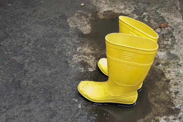 Photo of yellow rubber boots on rocks and asphalt, these shoes are usually worn by workers and farmers, these boots are waterproof