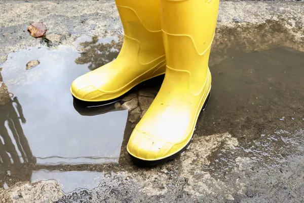 Photo of yellow rubber boots in a puddle of water, these shoes are usually worn by workers and farmers, these boots are waterproof
