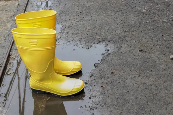 Photo of yellow rubber boots in a puddle of water, these shoes are usually worn by workers and farmers, these boots are waterproof
