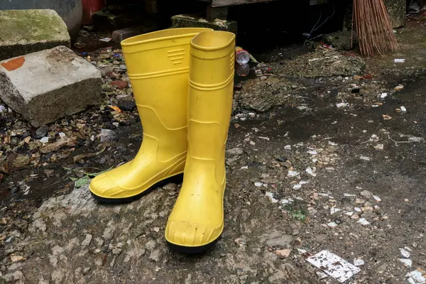Photo of yellow rubber boots on rocks and asphalt, these shoes are usually worn by workers and farmers, these boots are waterproof