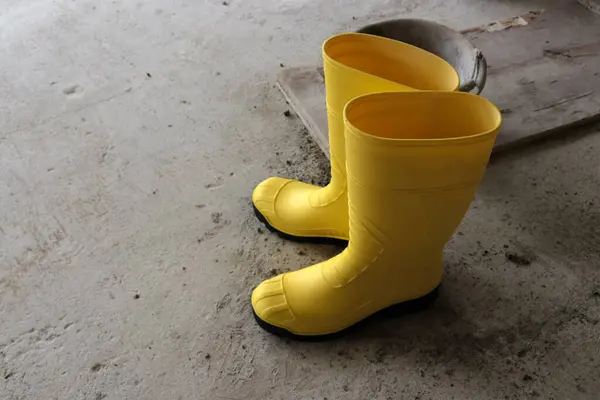 Photo of yellow rubber boots in a building under construction. These rubber boots are waterproof and are often used by construction workers