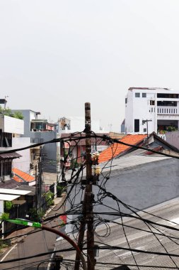 Küçük bir kasabada elektrik kablolarıyla dolu bir elektrik direğinin fotoğrafı.