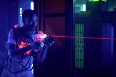 Lazer tag oyuncusu siyah ışıkta hafif silah bilimkurgu yeleği ateşliyor