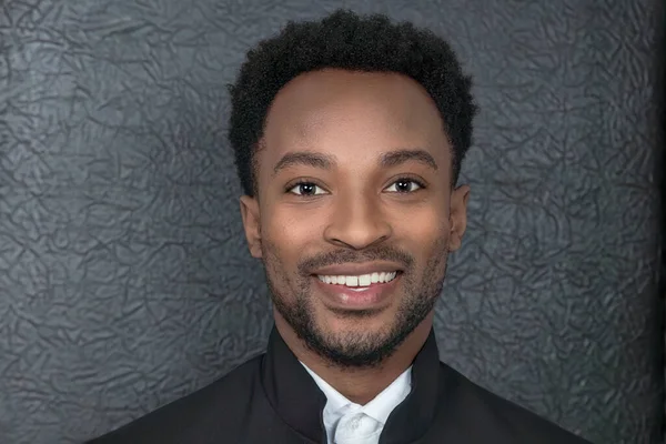 man smiling wearing black suit and white shirt in front of leather background, headshot of african man around twenty years old, smart and happy businessman
