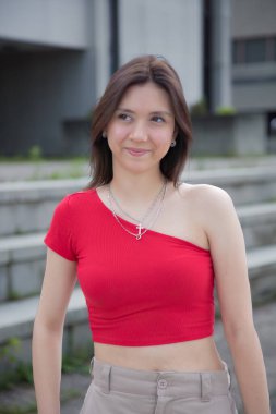 Genç model kadın canlı kırmızı bluzlu kaşkorse giyer. Kalçasında şehir hayatı var.
