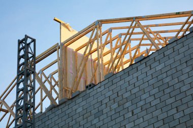 Yeni ev geliştirme ve mimari gelişimin sembolü olan inşaat alanında ahşap çatı çerçevesi mavi gökyüzüne karşı yükseliyor.
