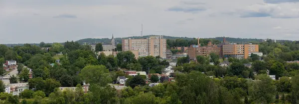 stock image A summer cityscape with an hospital, church and buildings in Sherbrooke, Quebec, and a natural urban landscape under an overcast sky and forest panorama.