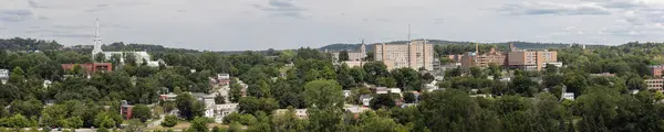 stock image A summer cityscape of downtown Sherbrooke, Quebec, featuring church, hospital, historic architecture, and a natural urban landscape under an overcast sky and forest panorama.