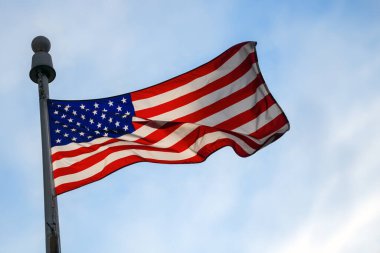 Görkemli bir Amerikan bayrağı bulutlu bir gökyüzüne karşı gururla dalgalanıyor. Güneş ışığı, vatanseverliği, özgürlüğü ve ulusal gururu simgeliyor. Bağımsızlık ve kutlama temaları için mükemmel.