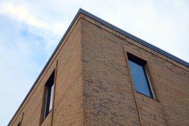 Parlak bir ofis kulesinin köşesinde mavi camlı pencereler, ışığı ve gökyüzünü yansıtan bir manzara. Bu çağdaş mimari tasarım kentsel gelişmişliği ve modern iş estetiğini vurgular..